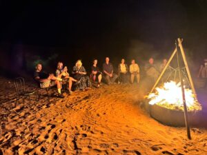 A group of people sit around a bonfire on chairs in the sand, a great way to create memories during a Marrakech destination wedding