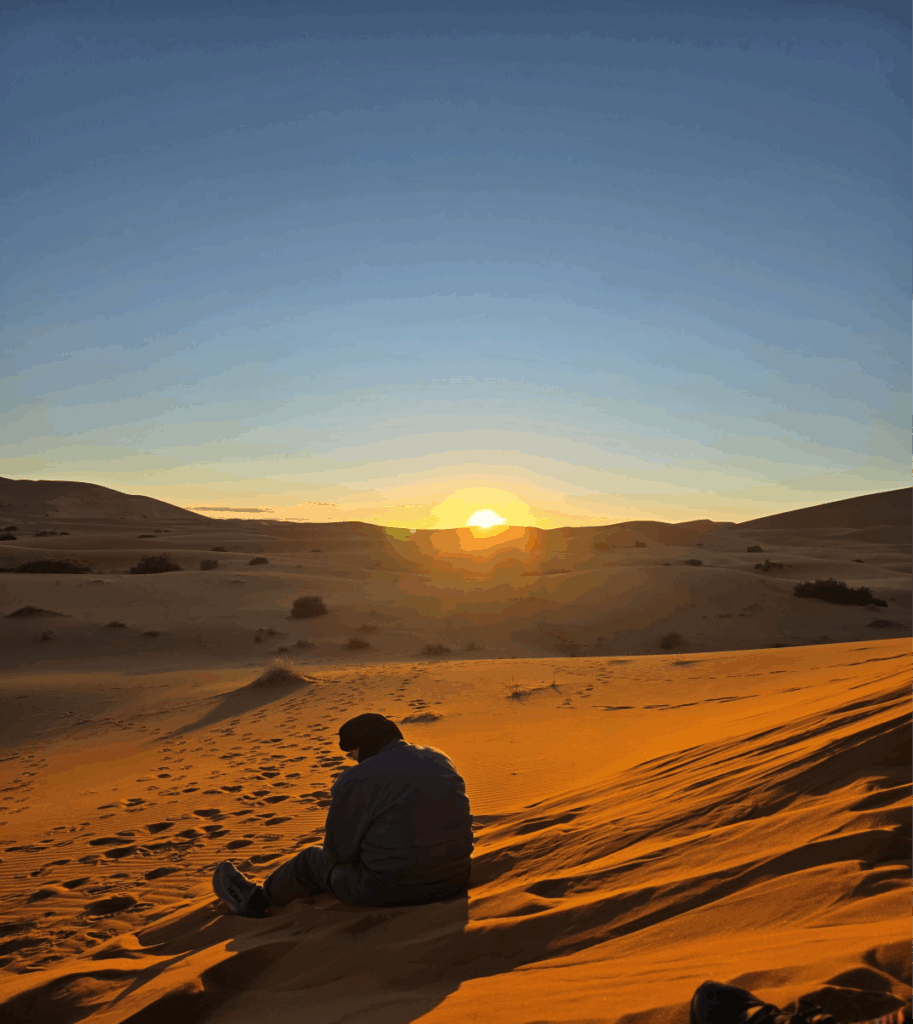 Person sitting in the Sahara Desert watching a s sunset
