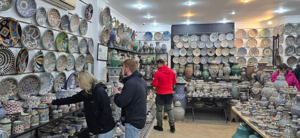 People browse and shop for colorful, intricately patterned ceramic plates and pottery inside a well-lit craft store.