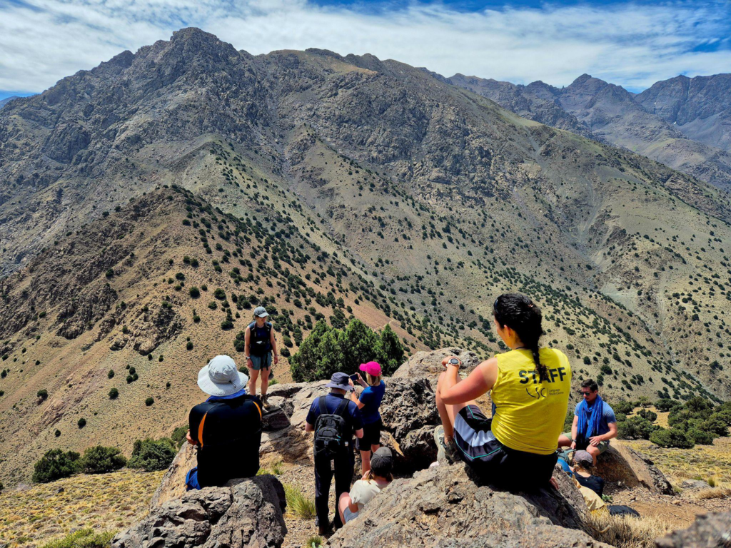  A group of hikers resting on a rocky mountain ridge, taking in sweeping views of rugged peaks and valleys.