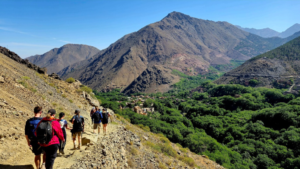 Group of hikers walking along a rocky mountain trail overlooking a green valley.